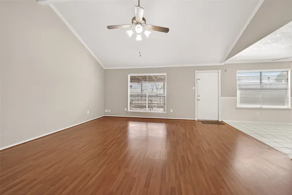 an empty room with wooden floor chandelier fan and windows
