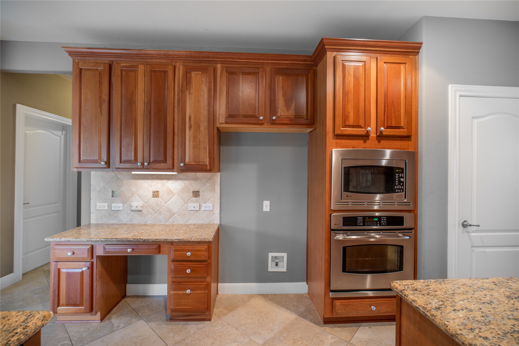 214 Summit Street Georgetown, TX 78633 - Photo 12 of 38 Kitchen featuring custom cabinetry, stainless steel microwave and oven, a built-in desk area, and granite countertops