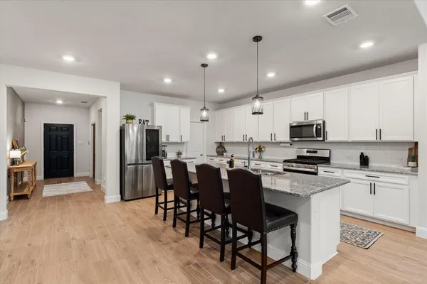 a kitchen with stainless steel appliances kitchen island granite countertop a sink a stove a microwave a island with cabinets and wooden floor