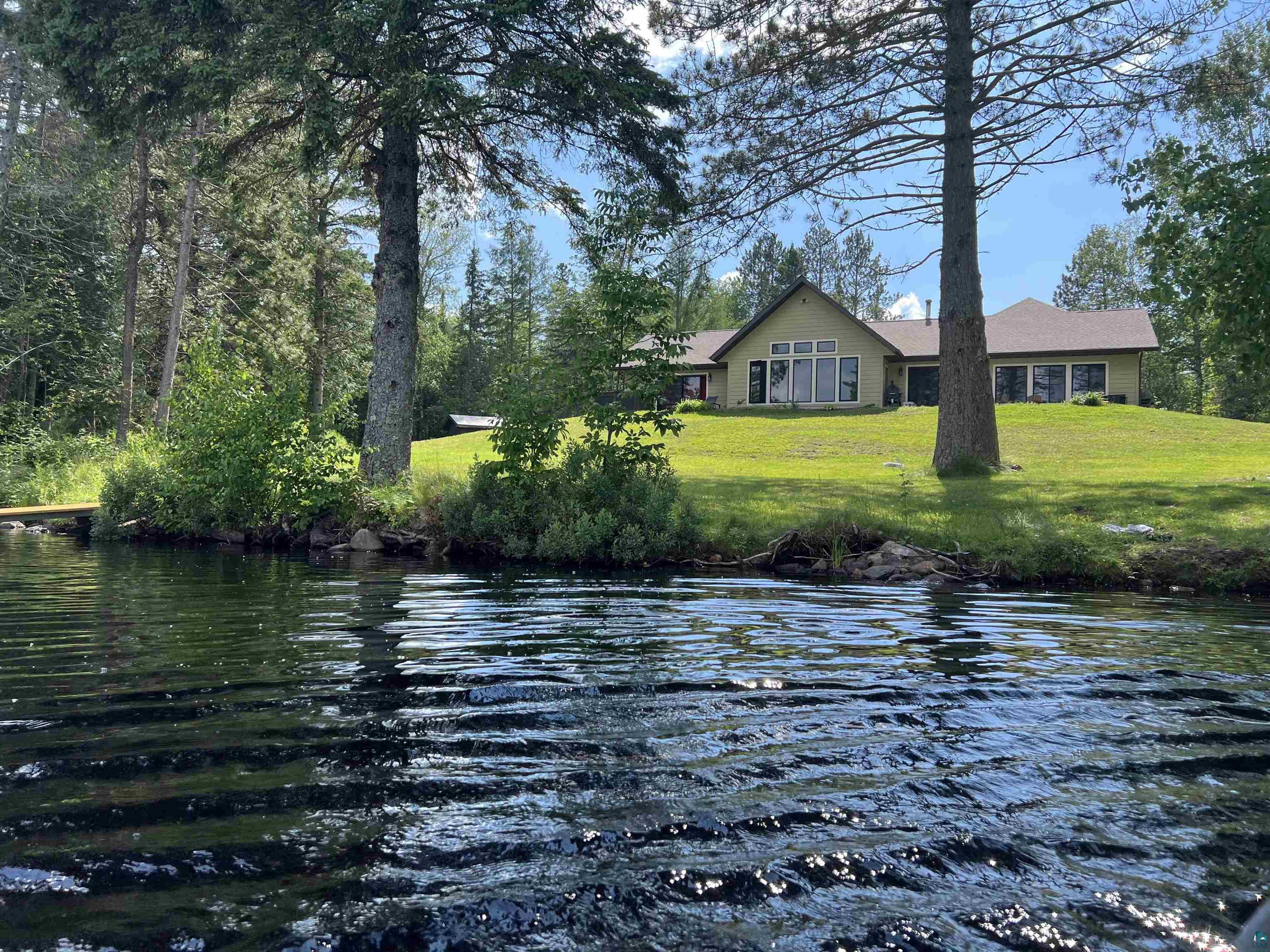 Waterfront property featuring a broad expanse of water, a verdant lawn, and mature trees framing a single-story residence