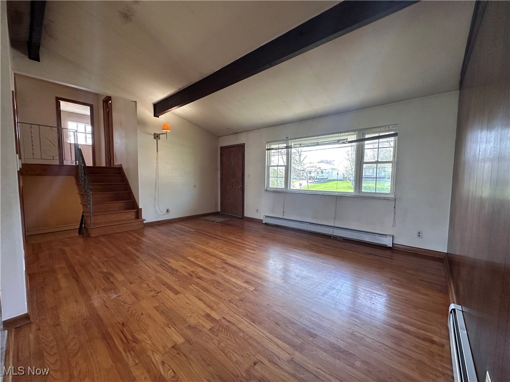 2829 Shellhart Road Barberton, OH 44203 - Photo 4 of 29 Unfurnished living room with a baseboard heating unit, wood finished floors, stairs, and lofted ceiling with beams