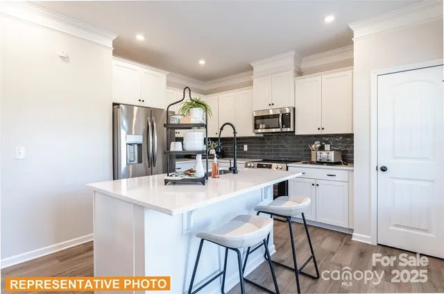 a kitchen with stainless steel appliances granite countertop a stove a sink a refrigerator a microwave and white cabinets with wooden floor