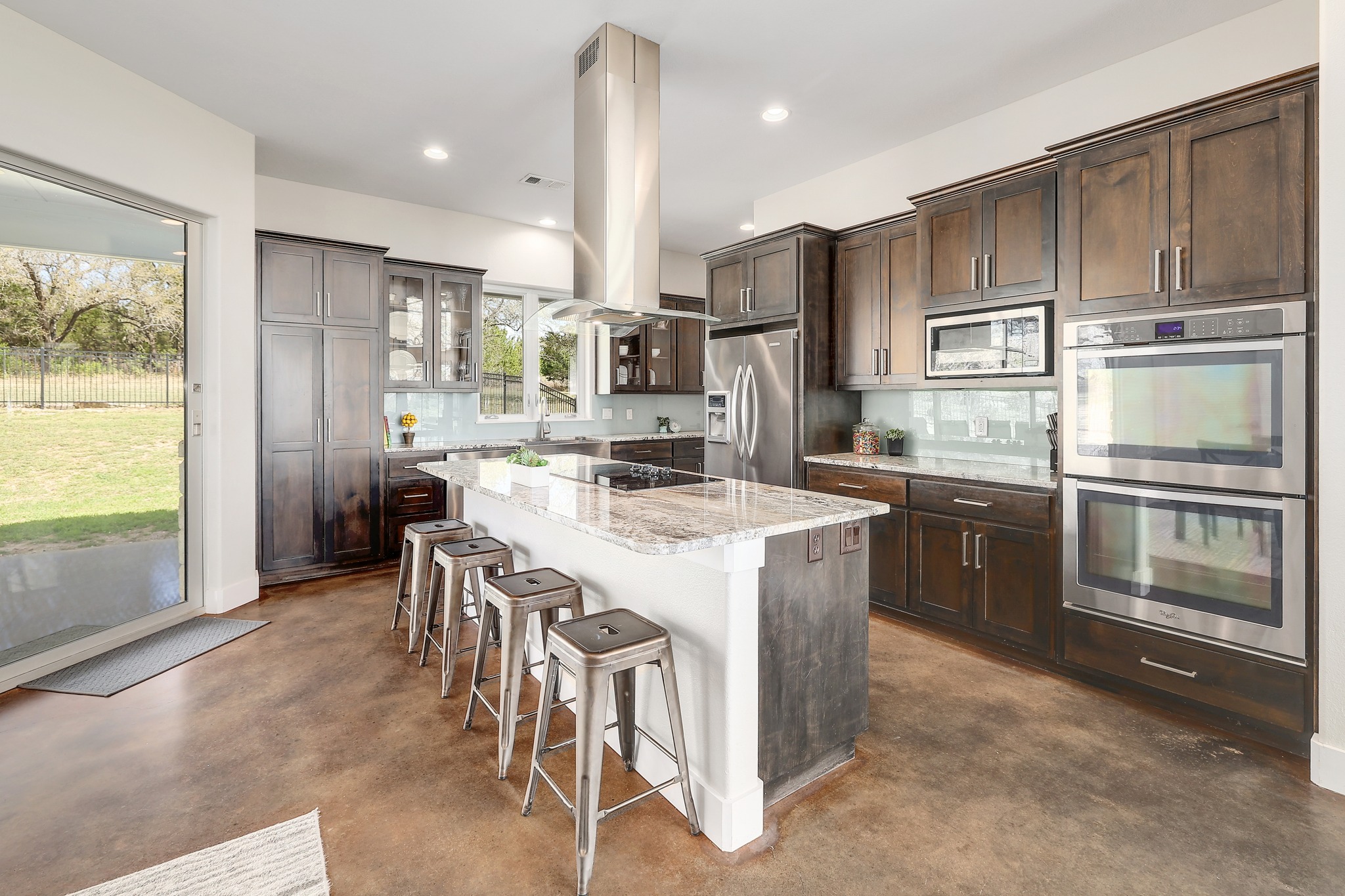 23928 Oscar Road Spicewood, TX 78669 - Photo 12 of 40 a kitchen with stainless steel appliances kitchen island granite countertop a refrigerator a stove a sink a dining table and chairs with wooden floor