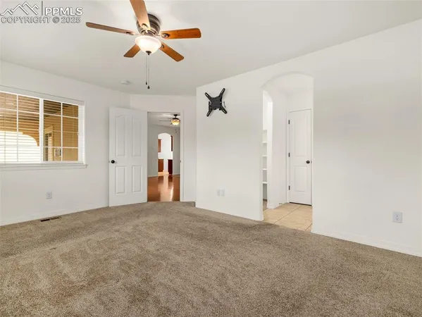 an empty room with chandelier fan and windows