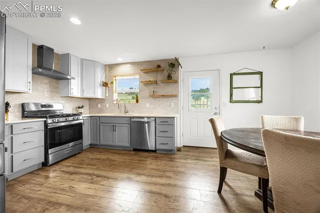 a kitchen with stainless steel appliances kitchen island granite countertop a stove a sink dishwasher a dining table and chairs with wooden floor