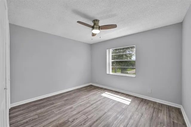 an empty room with wooden floor fan and windows