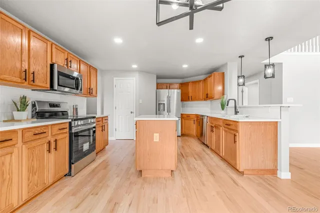 a large kitchen with stainless steel appliances kitchen island granite countertop a stove a sink a refrigerator and white cabinets with wooden floor