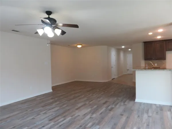 a view of an empty room with wooden floor and a ceiling fan