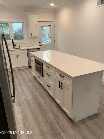 a room with kitchen island a sink dishwasher stove and white cabinets with wooden floor