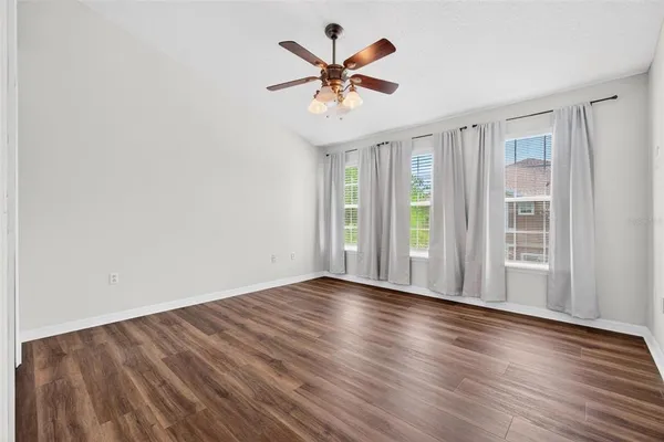 an empty room with wooden floor chandelier fan and windows