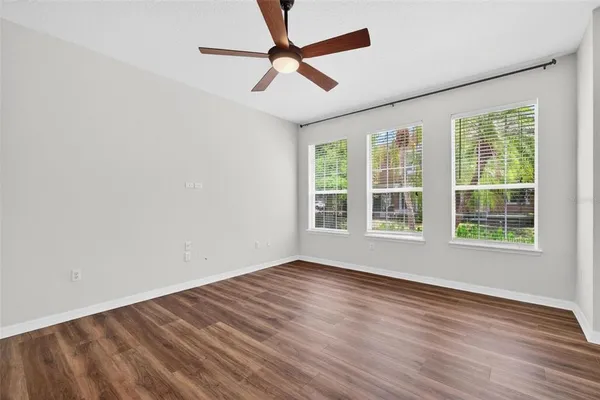 an empty room with wooden floor fan and windows