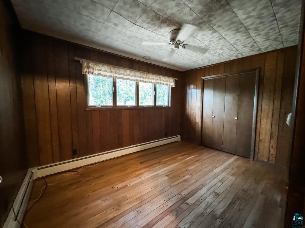 N13431 County Line Road Minong, WI 54859 - Photo 22 of 42 Empty room featuring wood-type flooring, ceiling fan, baseboard heating, and wooden walls