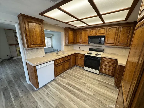 a kitchen with stainless steel appliances granite countertop a refrigerator a sink dishwasher a stove and white countertops with wooden floor