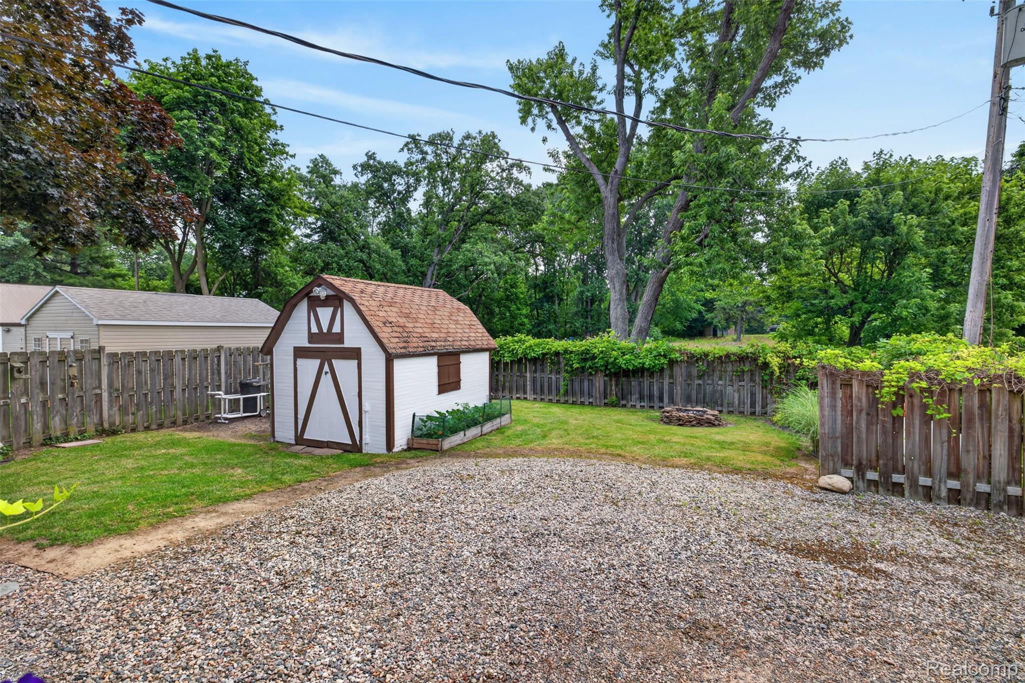 5977 Anglers Road Ortonville, MI 48462 - Photo 62 of 63 Expansive backyard featuring a white storage shed with a gambrel roof, gravel parking area, and wood privacy fencing