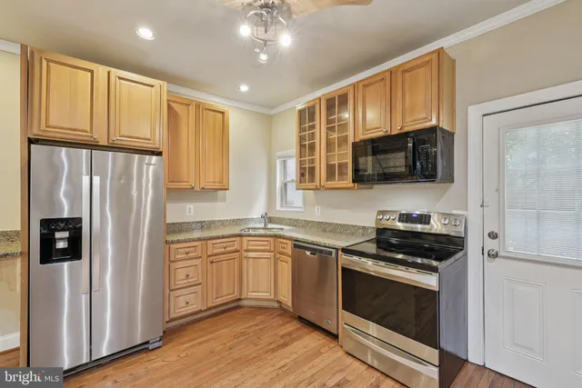 a kitchen with stainless steel appliances granite countertop a stove top oven a refrigerator a sink and dishwasher with wooden floor