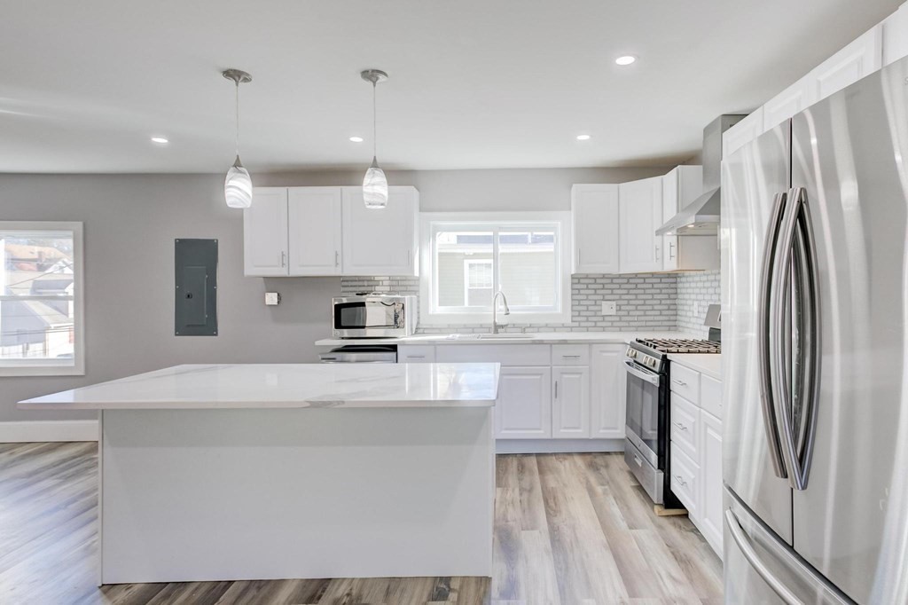 51 Prospect Street Woburn, MA 01801 - Photo 38 of 40 a large kitchen with a refrigerator a sink dishwasher a stove and white cabinets with wooden floor