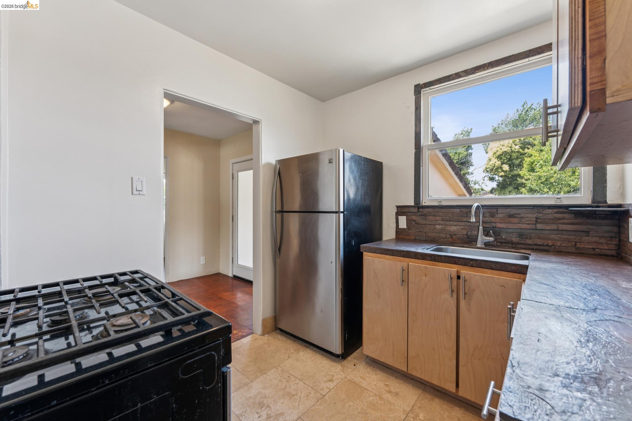 2879 Rheem Avenue Richmond, CA 94804 - Photo 22 of 45 Kitchen featuring a large window, stacked stone backsplash, stainless steel refrigerator, black gas range, and wood-finish cabinetry