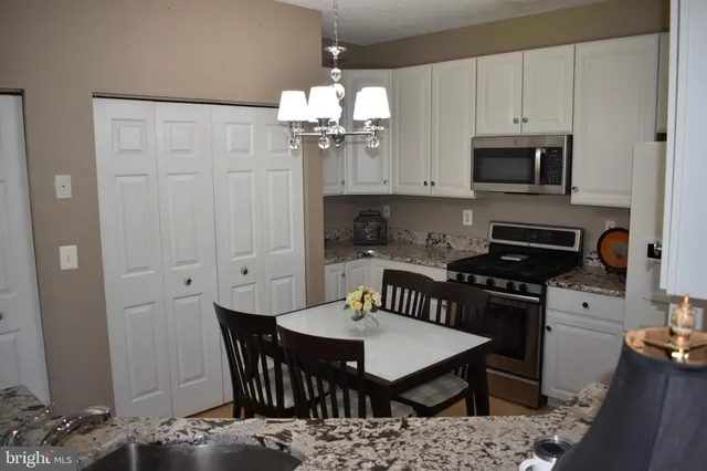 a kitchen with stainless steel appliances kitchen island granite countertop a dining table chairs and a refrigerator