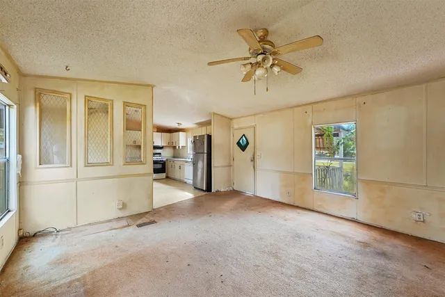 an empty room with chandelier fan and windows