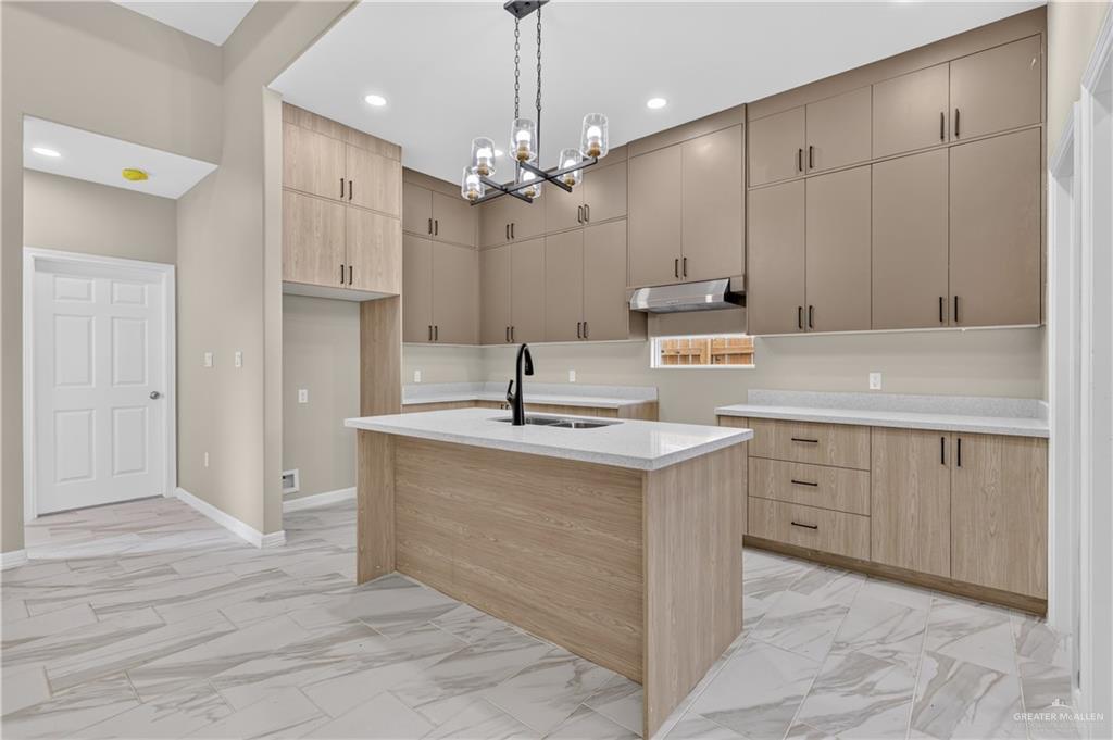 1920 Trinity Street Donna, TX 78537 - Photo 9 of 23 Modern kitchen featuring an island with a built-in sink, light wood-finish cabinetry, matte taupe upper cabinetry, white countertops, and large format tile flooring