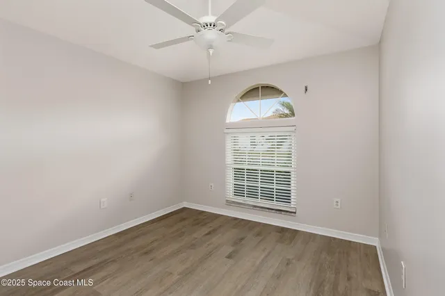 an empty room with wooden floor ceiling fan and windows