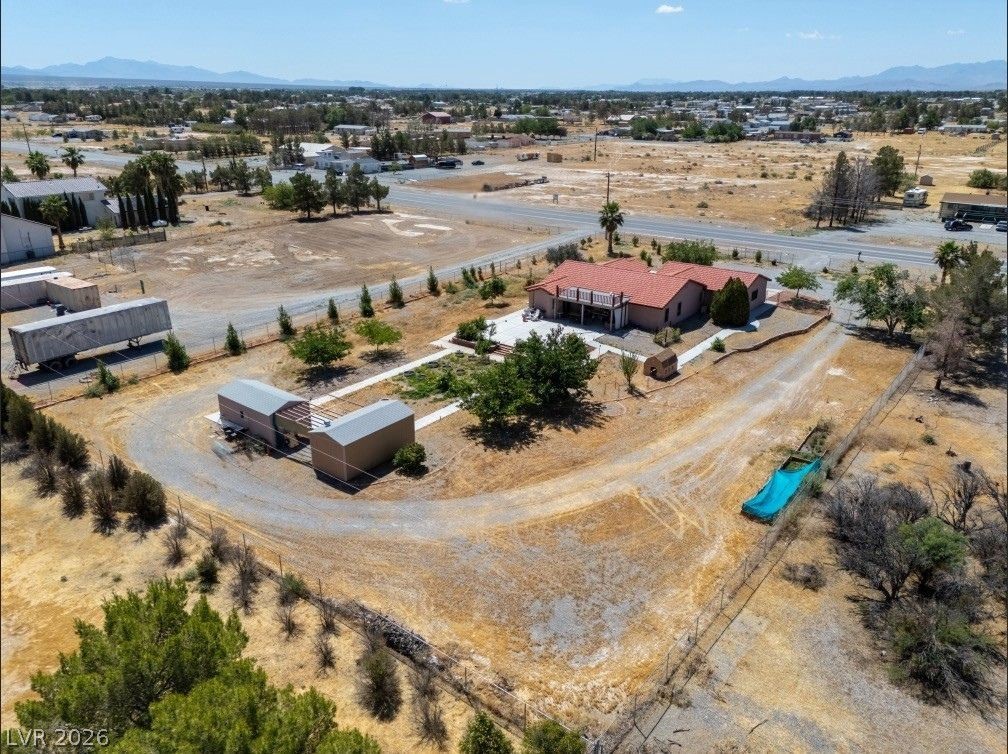 1220 East Gamebird Road Pahrump, NV 89048 - Photo 48 of 49 An aerial perspective reveals a spacious property featuring a house with a balcony, multiple outbuildings, and an open, dry landscape.