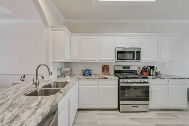 a kitchen with white cabinets a sink stove and microwave oven with wooden floor