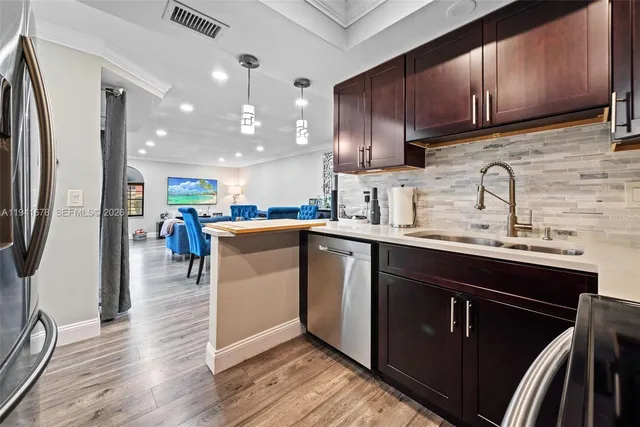 a kitchen with stainless steel appliances granite countertop a refrigerator a sink dishwasher a stove and white countertops with wooden floor