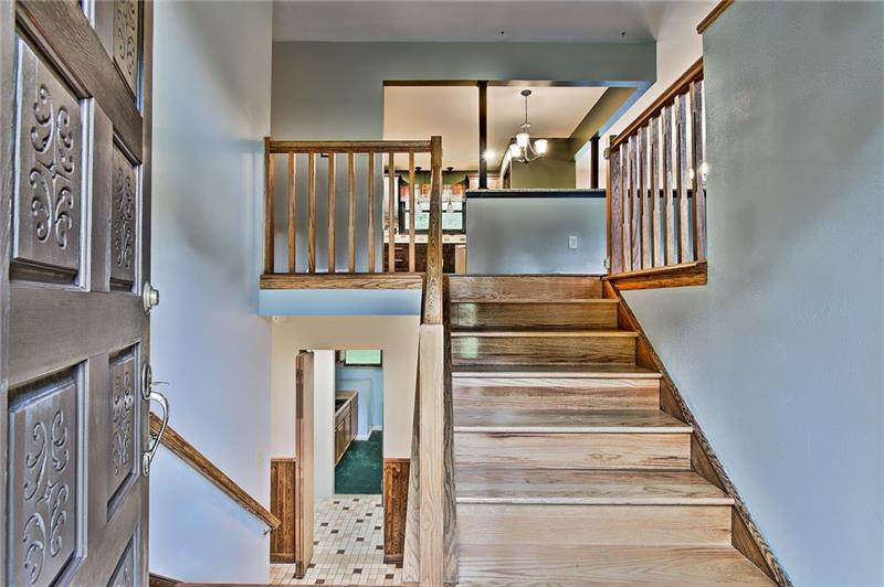 112 Wycliffe Way Butler, PA 16001 - Photo 9 of 24 Main entry at mid-level. Wooden stairs flanked by oak railings. Bonus info: See that checkered floor and the green floor to the left of the steps? The checkered floor is a full bath and the green floor is a SECOND kitchen! Yes, this house has 2 kitchens. Perfect for having EVERYONE over for the holidays, even the in laws! Turkey in the oven upstairs, and ham down below. Includes an old, but interesting looking stove/oven, fridge, counter space, sink and newer stainless full-size freezer.