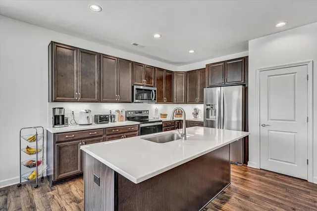 a kitchen with stainless steel appliances granite countertop a refrigerator a sink dishwasher a stove and white countertops with wooden floor