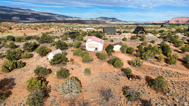 358 South Sky Drive Torrey, UT 84775 - Photo 45 of 82 Expansive desert landscape featuring multiple structures, including a primary residence with a red roof, various outbuildings, and two A-frame houses