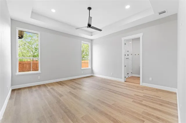 an empty room with wooden floor ceiling fan and windows