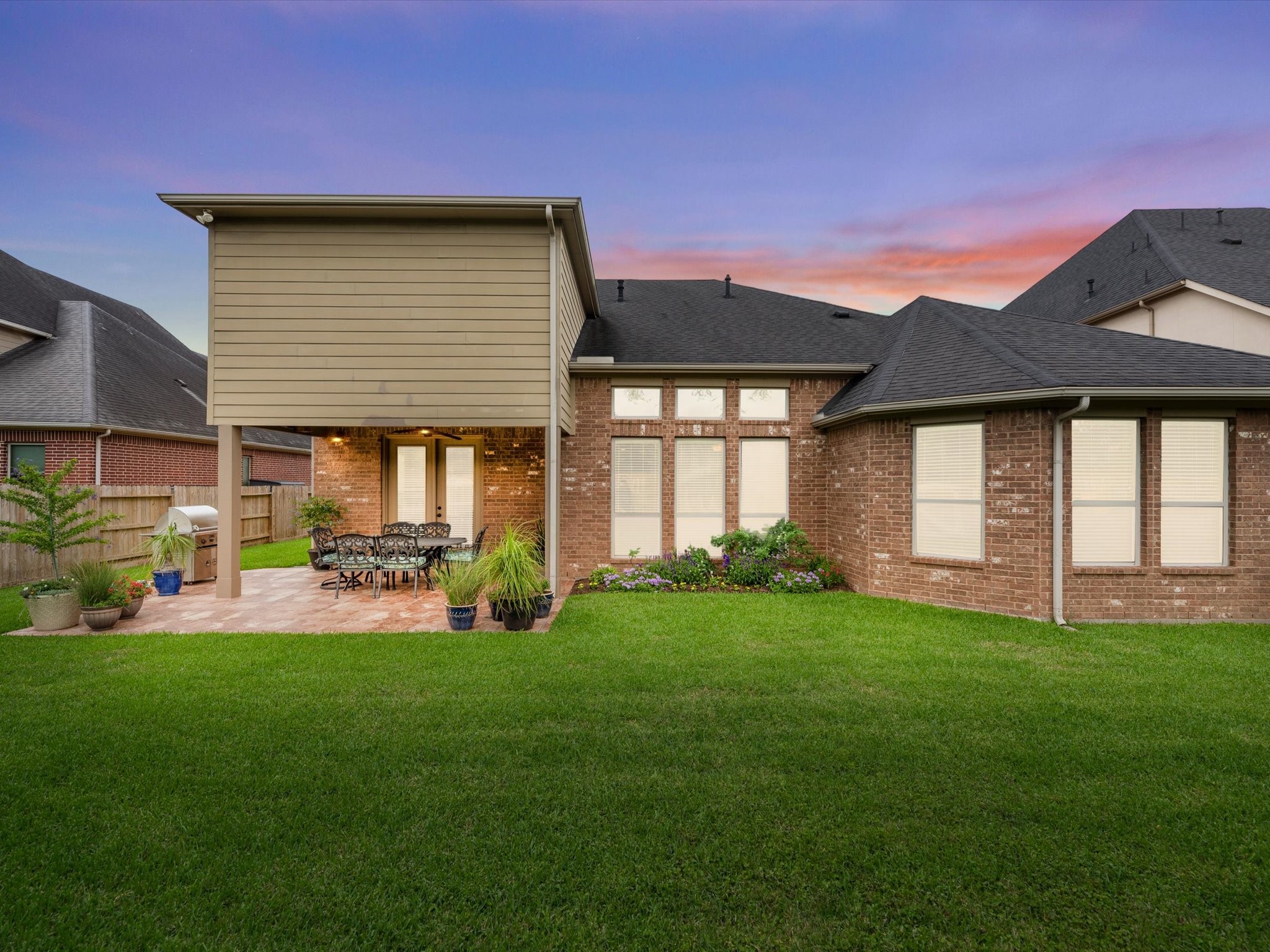 3907 Randle Ridge Court Fulshear, TX 77441 - Photo 40 of 46 This photo showcases a spacious backyard with a well-maintained lawn, a brick exterior, rear yard landscape lighting, and a covered patio area perfect for outdoor dining and relaxation. The twilight sky adds a warm, inviting ambiance.