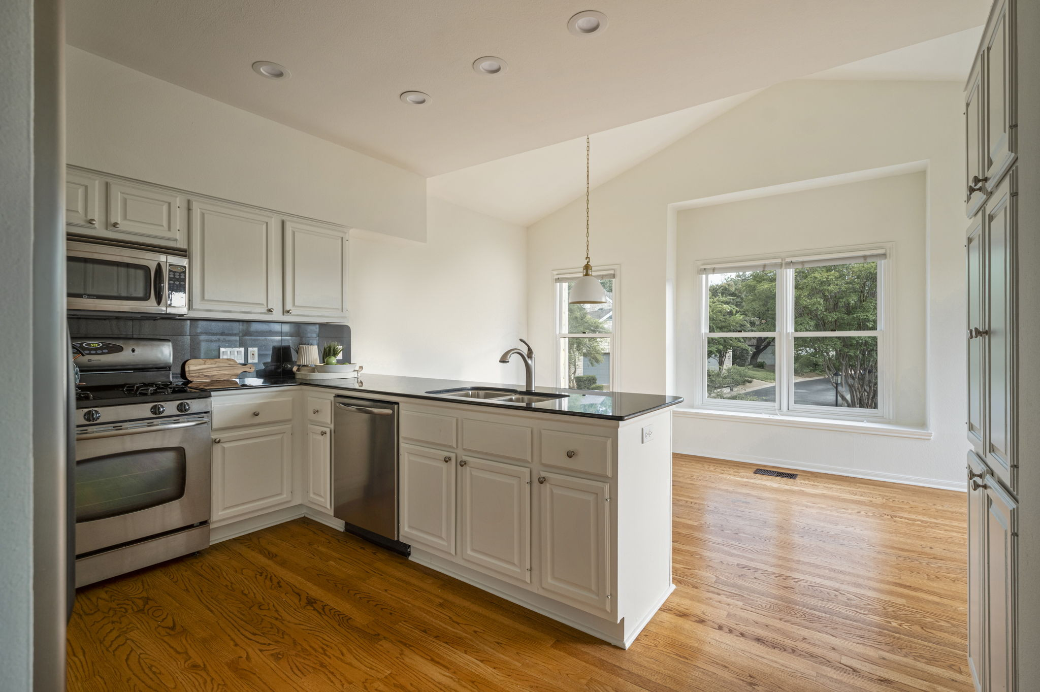6010 Long Champ Court, Unit 113 Austin, TX 78746 - Photo 11 of 25 Kitchen with a peninsula, vaulted ceiling, tasteful backsplash, stainless steel appliances, and light wood finished floors