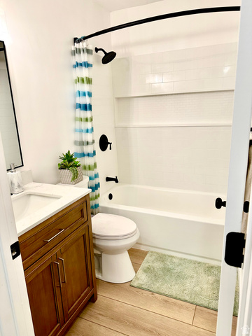7818 North Windhover Road Eagle Mountain, UT 84005 - Photo 19 of 32 Bathroom featuring a white subway tile surround, matte black fixtures, a built-in shower shelf, a white vanity with a rectangular sink, and wood-finish flooring