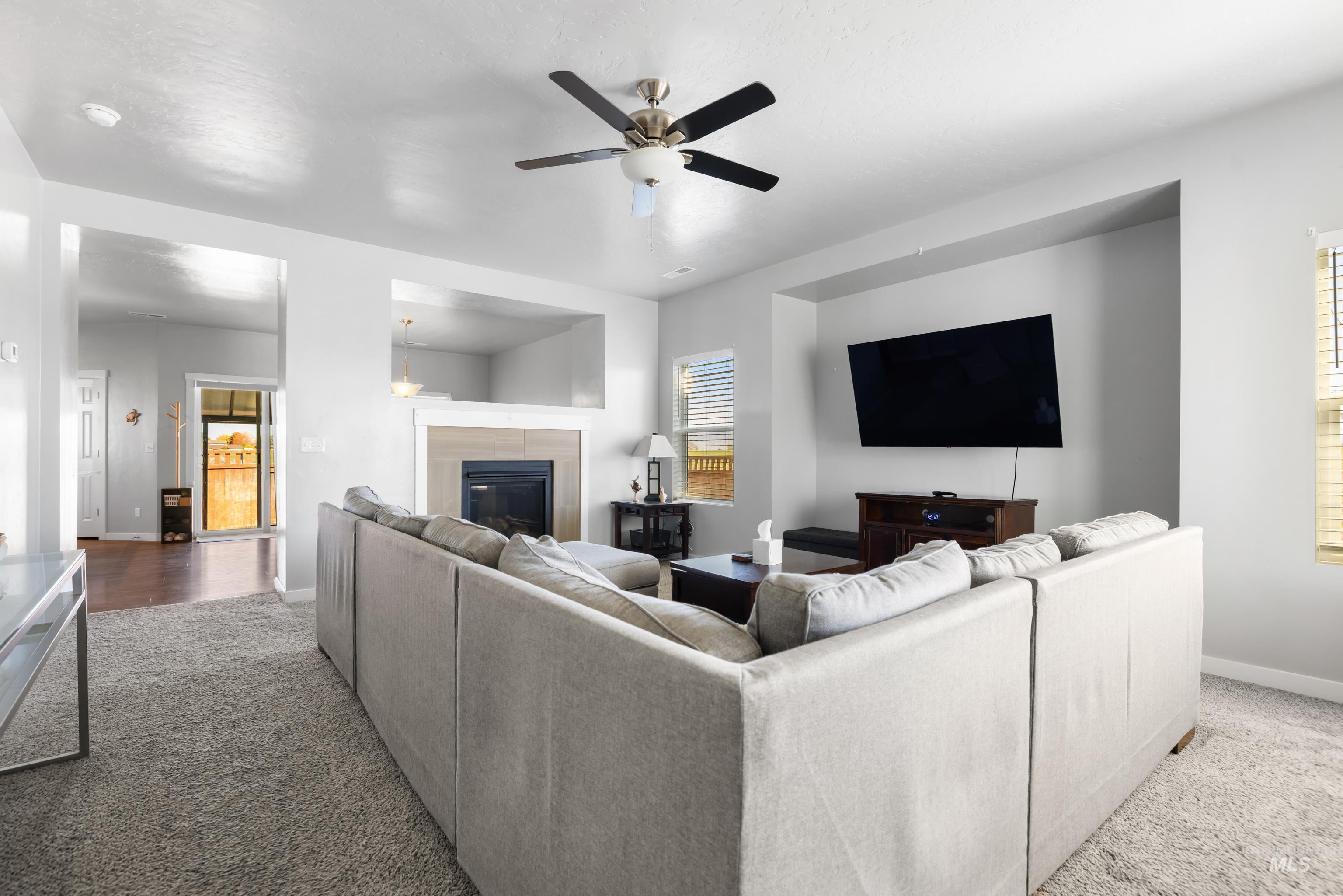 6988 West Spur Street Boise, ID 83709 - Photo 11 of 37 Living area with a glass covered fireplace, carpet flooring, and a ceiling fan