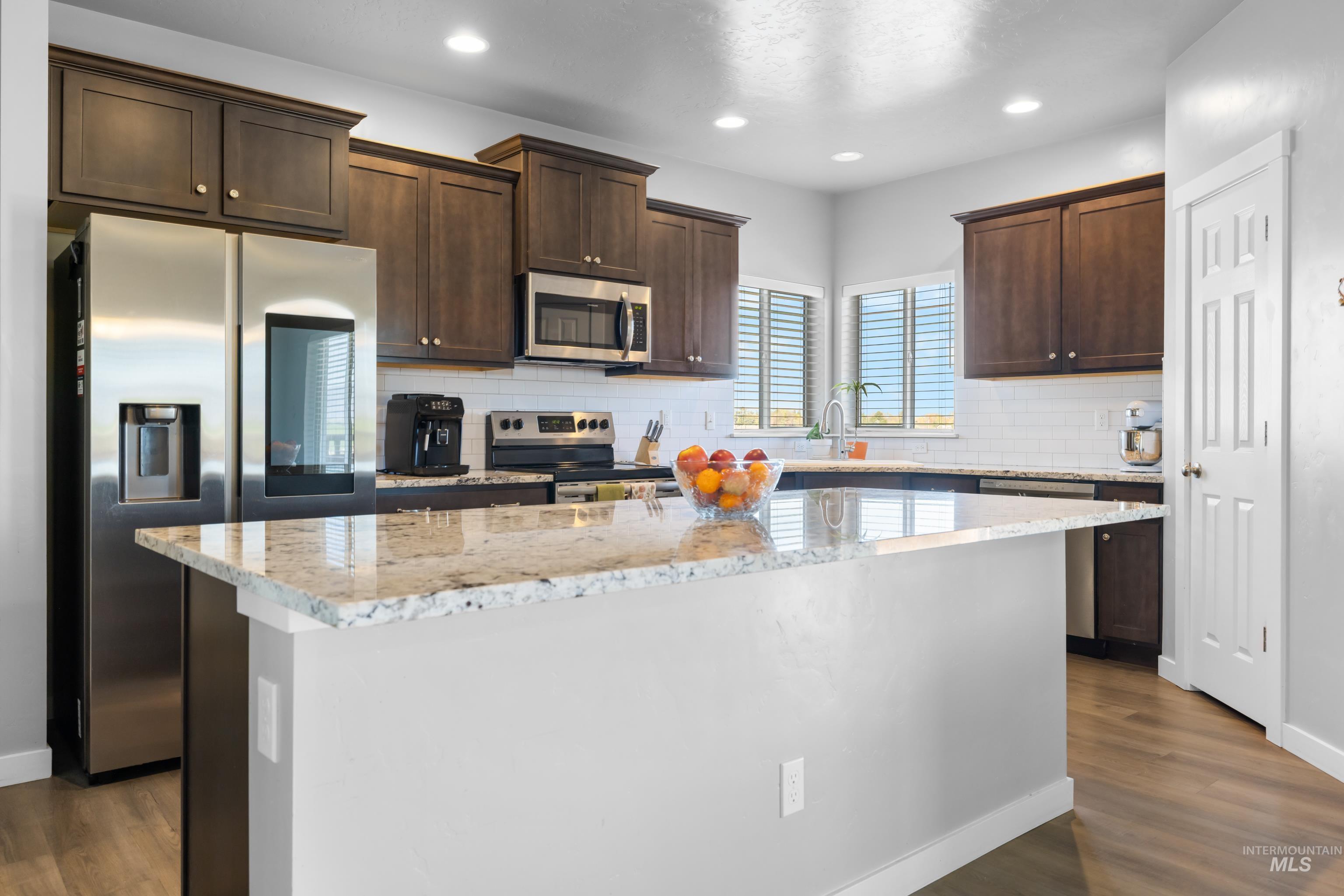 6988 West Spur Street Boise, ID 83709 - Photo 14 of 37 Kitchen with light stone counters, stainless steel appliances, dark wood finish cabinetry, a kitchen island, and dark wood finished floors