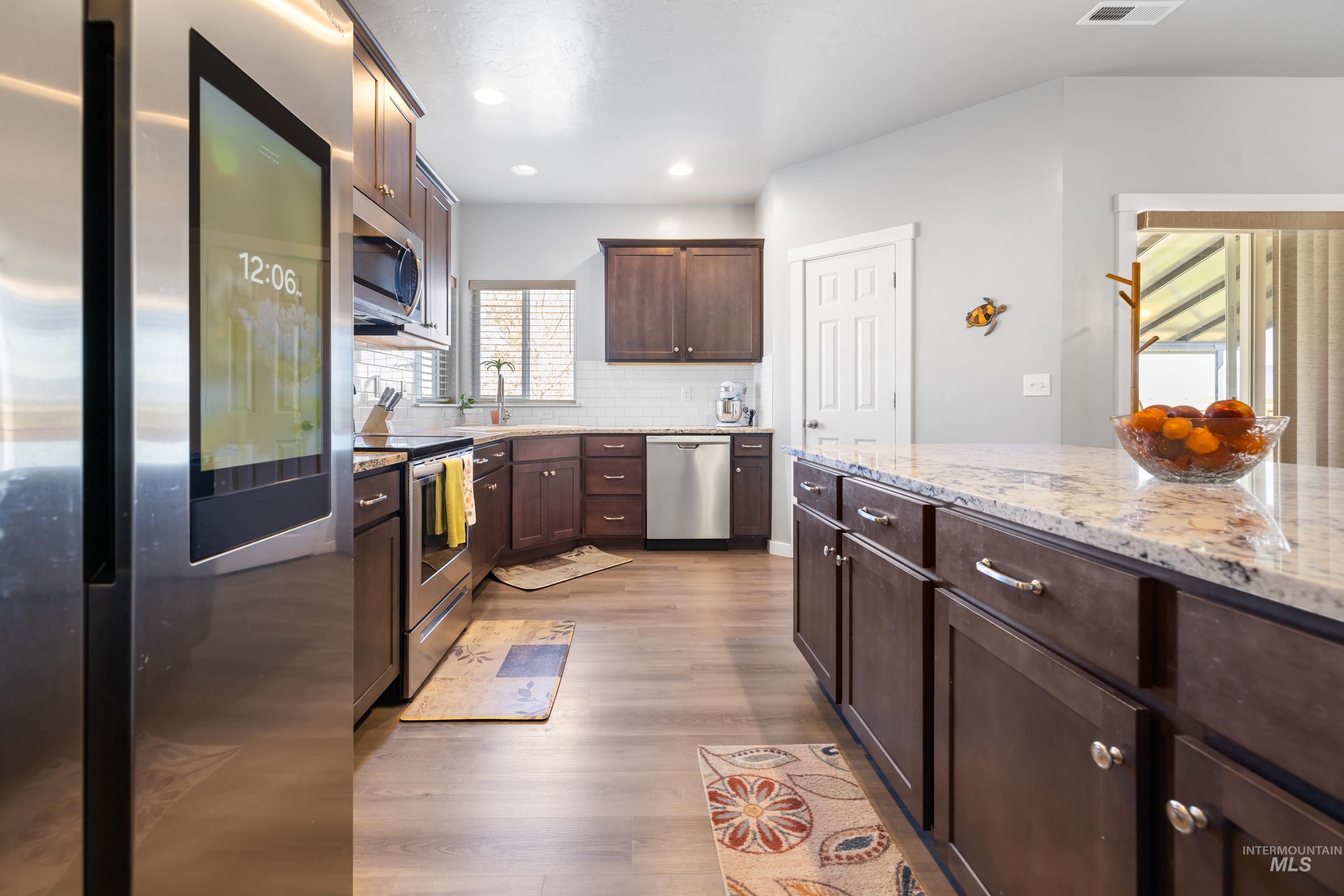 6988 West Spur Street Boise, ID 83709 - Photo 9 of 37 Kitchen with stainless steel appliances, dark wood finish cabinets, light stone countertops, dark wood-type flooring, and decorative backsplash