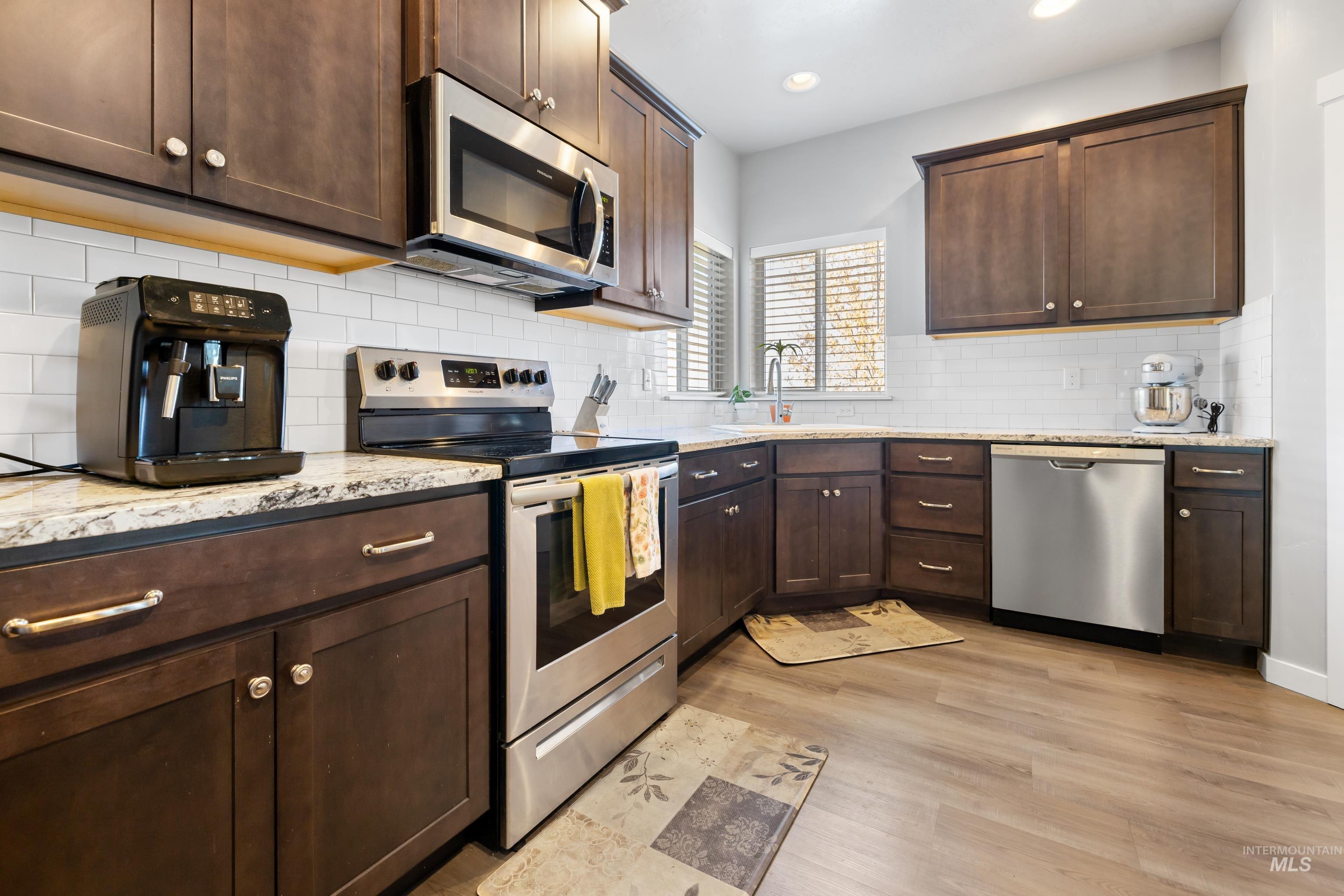 6988 West Spur Street Boise, ID 83709 - Photo 10 of 37 Kitchen with stainless steel appliances, dark wood finish cabinetry, light stone countertops, light wood-style flooring, and recessed lighting