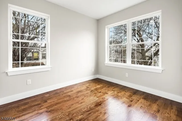 a view of an empty room with wooden floor and windows