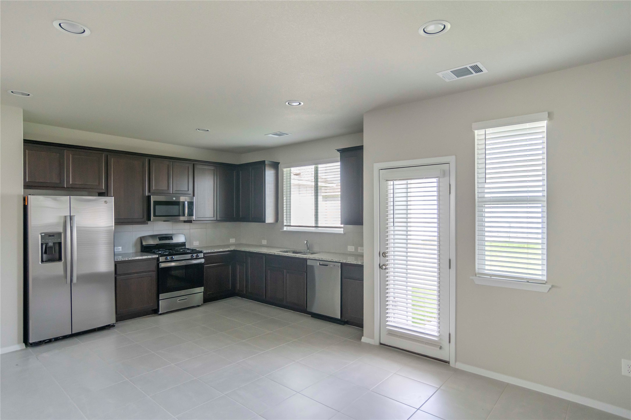 1257 Goforth Road Kyle, TX 78640 - Photo 6 of 33 Kitchen with stainless steel appliances, dark wood finish cabinetry, light tile patterned floors, recessed lighting, and tasteful backsplash