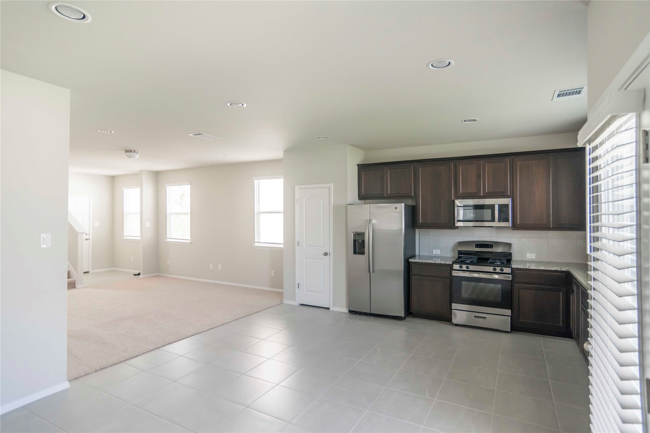 1257 Goforth Road Kyle, TX 78640 - Photo 33 of 33 Kitchen with stainless steel appliances, dark wood finish cabinets, light carpet, open floor plan, and light tile patterned floors