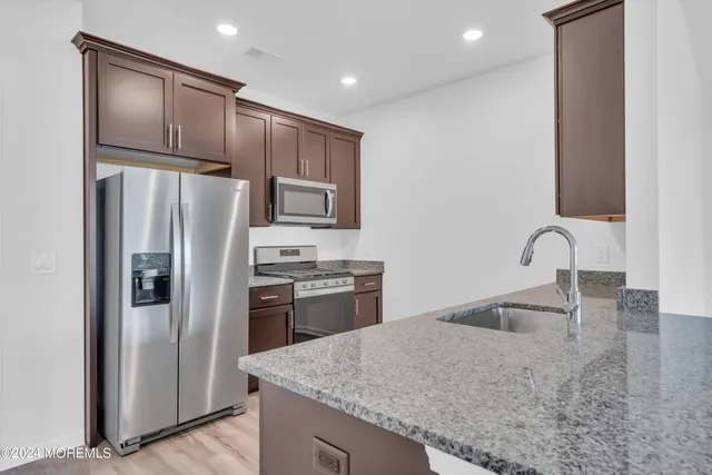 a kitchen with stainless steel appliances granite countertop a refrigerator a stove and a sink with wooden floors