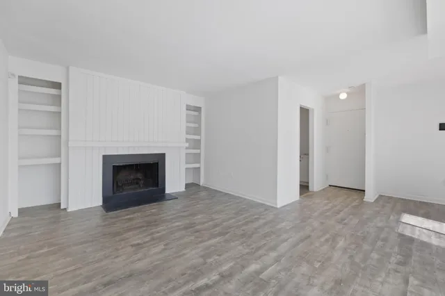 a view of an empty room with wooden floor fireplace and a window