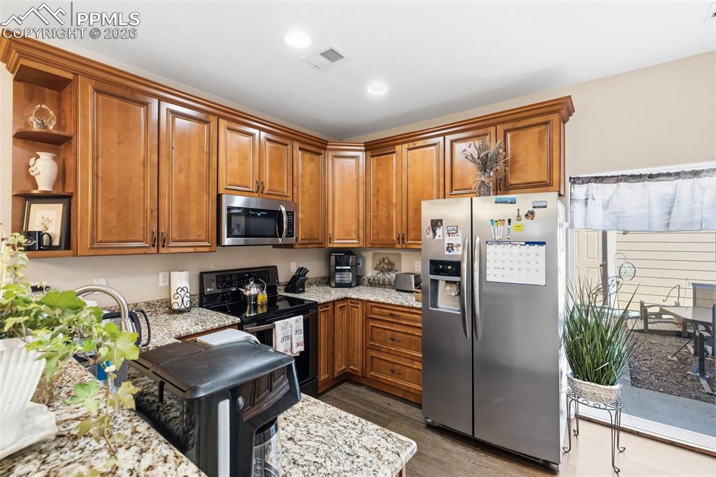 3519 Grey Owl Point Colorado Springs, CO 80916 - Photo 9 of 29 Kitchen featuring stainless steel appliances, wood finish cabinets, open shelves, light stone countertops, and recessed lighting