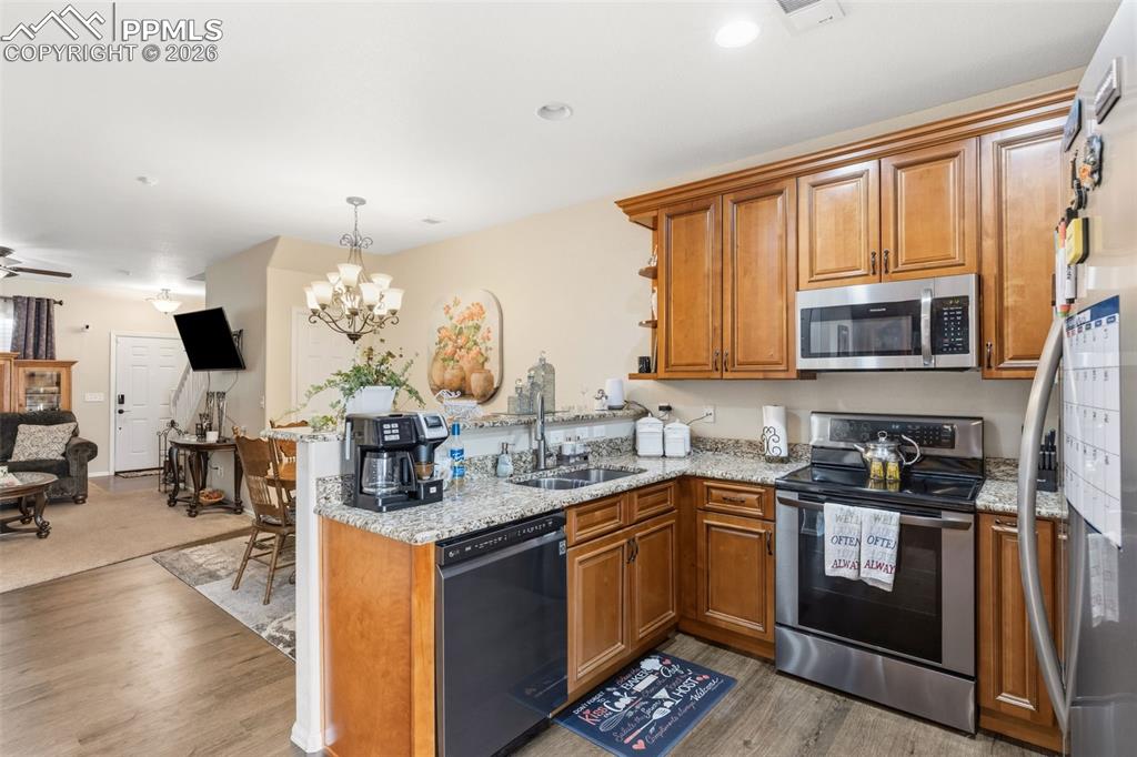 3519 Grey Owl Point Colorado Springs, CO 80916 - Photo 10 of 29 Kitchen featuring wood finish cabinetry, stainless steel appliances, a peninsula, and a chandelier