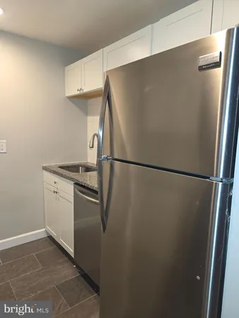 a view of a refrigerator in kitchen and an empty room in wooden floor