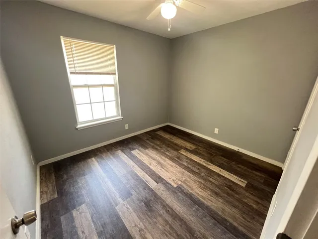 an empty room with wooden floor chandelier fan and windows