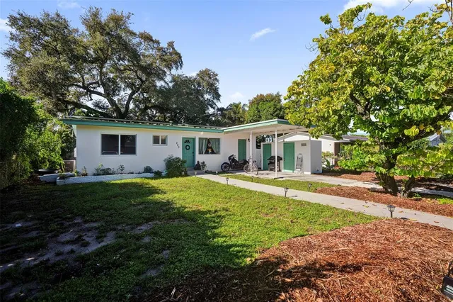 a white house with a yard plants and large tree