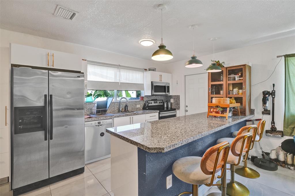 220 Northeast 165th Street Miami, FL 33162 - Photo 6 of 26 a kitchen with stainless steel appliances granite countertop a refrigerator a stove a sink a dining table and chairs with wooden floor